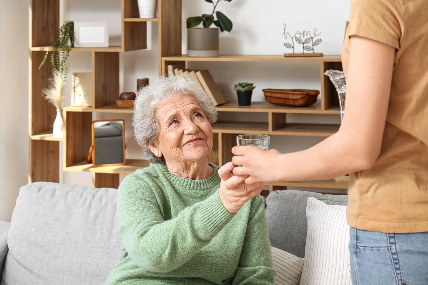 Seniorin zu Hause, eine Betreuerin reicht ihr ein Glas Wasser